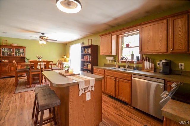 kitchen with a kitchen bar, sink, light wood-type flooring, stainless steel dishwasher, and a center island