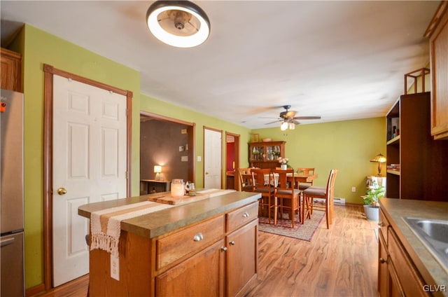 kitchen with stainless steel fridge, ceiling fan, light wood-type flooring, a kitchen island, and sink