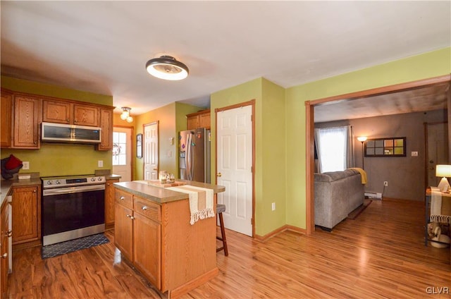 kitchen with light hardwood / wood-style floors, a kitchen bar, stainless steel appliances, a healthy amount of sunlight, and a center island