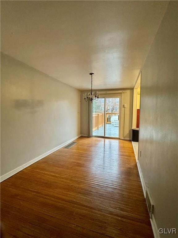 spare room with a notable chandelier and hardwood / wood-style flooring