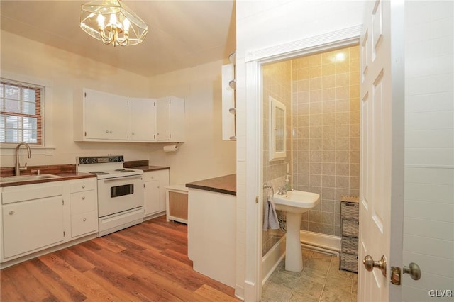 kitchen with sink, hanging light fixtures, white range with electric cooktop, white cabinets, and a chandelier