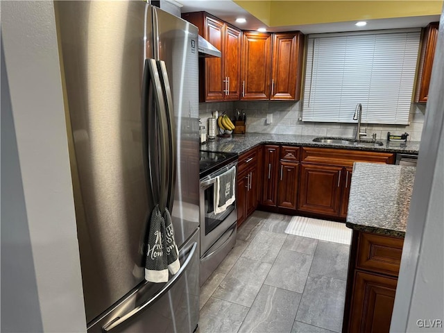 kitchen with appliances with stainless steel finishes, decorative backsplash, dark stone counters, wall chimney exhaust hood, and sink