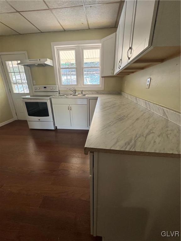 kitchen featuring a drop ceiling, white range with electric stovetop, sink, dark wood-type flooring, and white cabinets