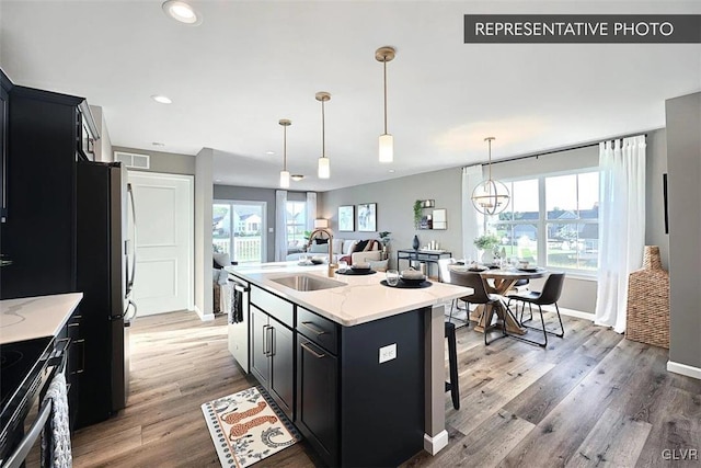 kitchen with sink, hardwood / wood-style flooring, hanging light fixtures, a kitchen island with sink, and light stone counters