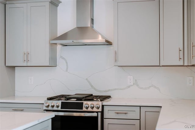 kitchen featuring decorative backsplash, gray cabinetry, gas stove, light stone countertops, and wall chimney range hood