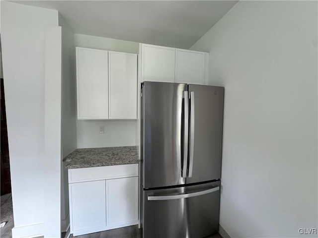 kitchen featuring white cabinets, dark stone counters, and stainless steel refrigerator