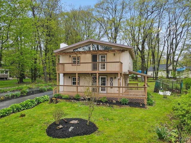 rear view of house with a balcony, a wooden deck, and a lawn