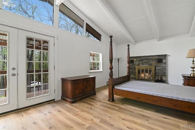 interior space with high vaulted ceiling, beam ceiling, a stone fireplace, and light wood-type flooring