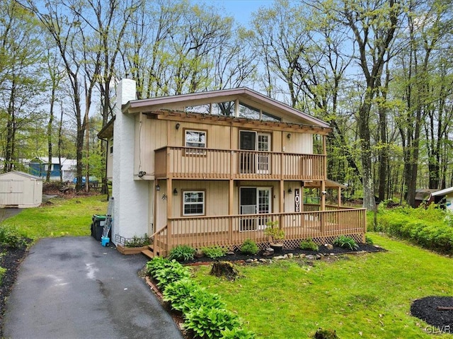 rear view of property featuring a shed, a balcony, and a yard