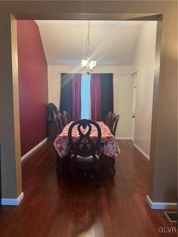 dining space featuring vaulted ceiling, dark hardwood / wood-style floors, and an inviting chandelier