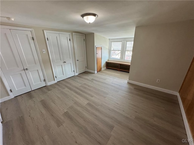 unfurnished bedroom with light wood-type flooring and multiple closets