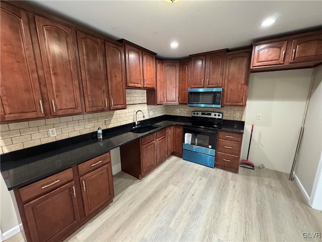 kitchen featuring sink, light hardwood / wood-style flooring, stainless steel appliances, and dark stone countertops