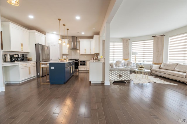 kitchen with wall chimney range hood, a center island, appliances with stainless steel finishes, a breakfast bar area, and white cabinets