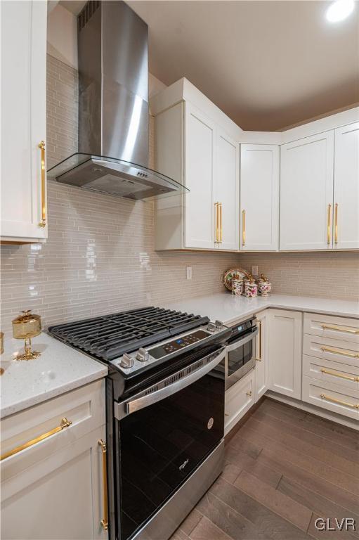 kitchen with wall chimney range hood, white cabinetry, dark wood-type flooring, light stone counters, and gas range