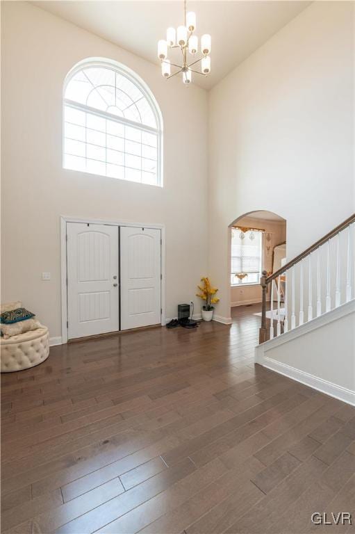 entryway with an inviting chandelier, a towering ceiling, and dark wood-type flooring