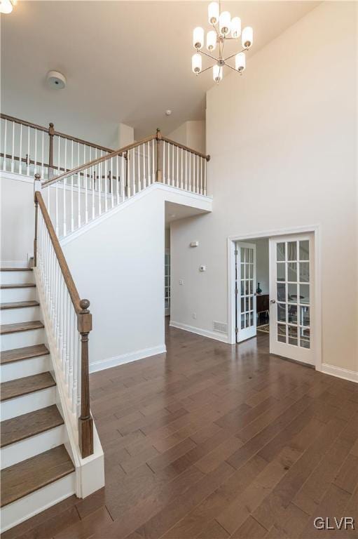 stairway with wood-type flooring, a notable chandelier, french doors, and a high ceiling