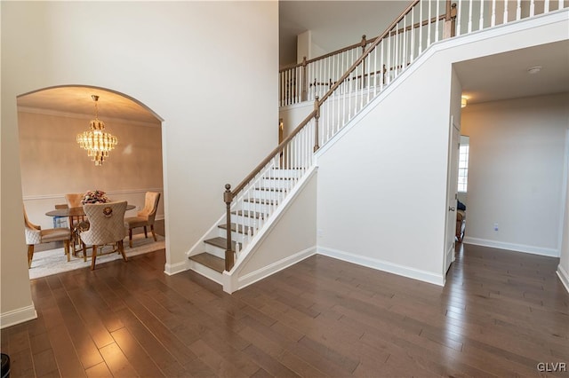 staircase with crown molding, a high ceiling, a chandelier, and hardwood / wood-style floors