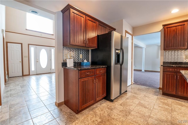 kitchen with light colored carpet, stainless steel fridge, dark stone counters, and tasteful backsplash