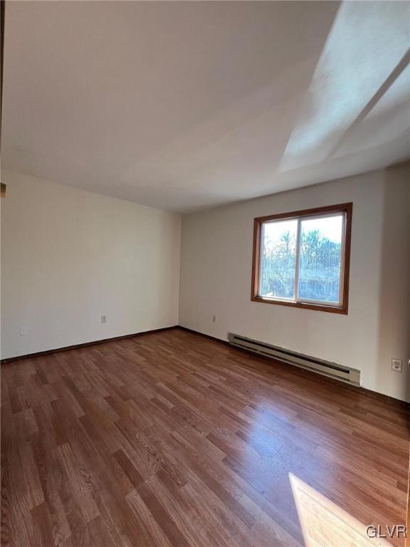 unfurnished room with baseboard heating and wood-type flooring