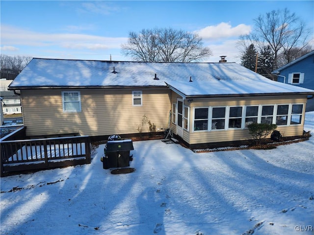 snow covered house featuring a wooden deck and a sunroom