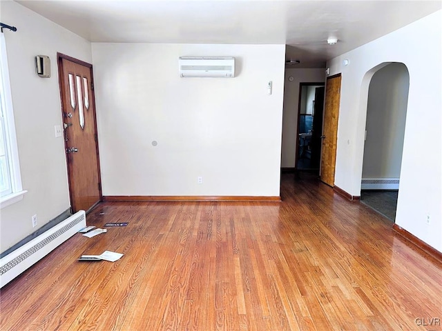 empty room featuring an AC wall unit, hardwood / wood-style flooring, and a baseboard heating unit