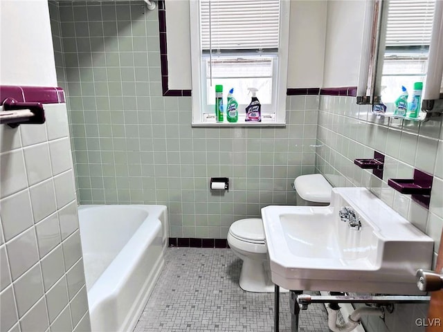 bathroom featuring toilet, tile walls, tile patterned floors, a tub to relax in, and sink