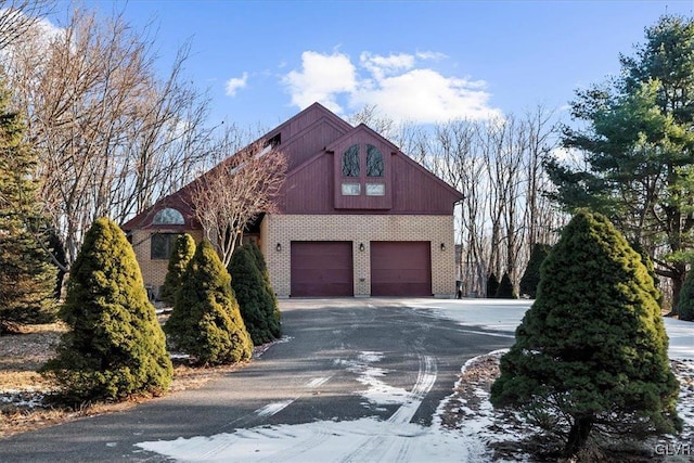 view of property exterior with brick siding, an attached garage, and aphalt driveway