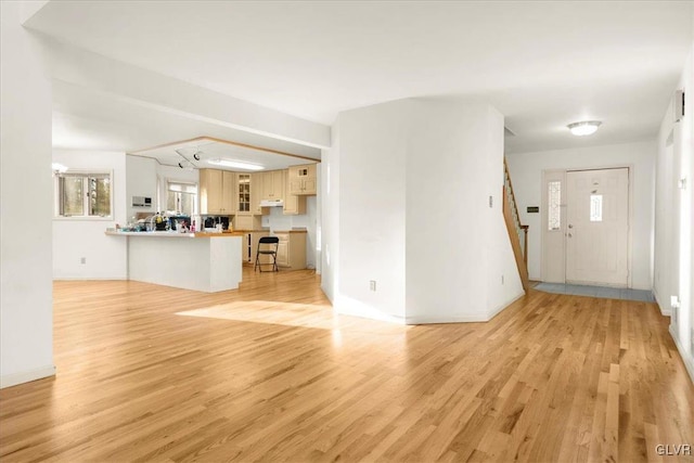 unfurnished living room with baseboards, stairway, and light wood-style floors