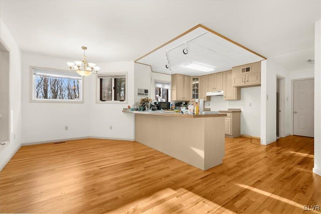 kitchen with light hardwood / wood-style floors, hanging light fixtures, kitchen peninsula, cream cabinets, and a chandelier