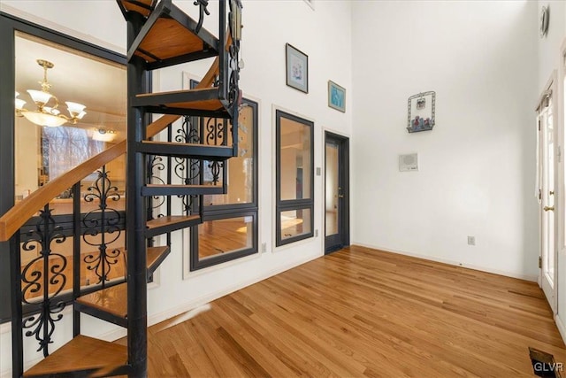 interior space with a notable chandelier, wood finished floors, a towering ceiling, baseboards, and stairs