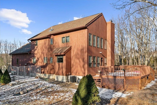 snow covered rear of property featuring fence, a chimney, a wooden deck, and central AC unit