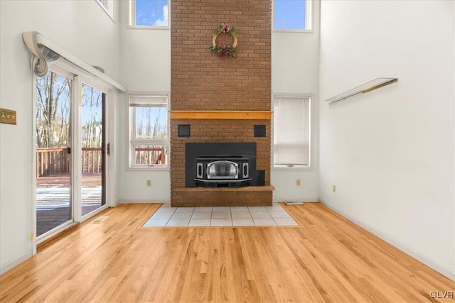 unfurnished living room with visible vents, light wood-style flooring, a towering ceiling, and a wealth of natural light