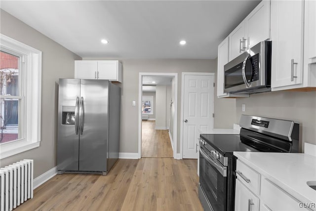 kitchen with stainless steel appliances, a healthy amount of sunlight, white cabinetry, and radiator heating unit