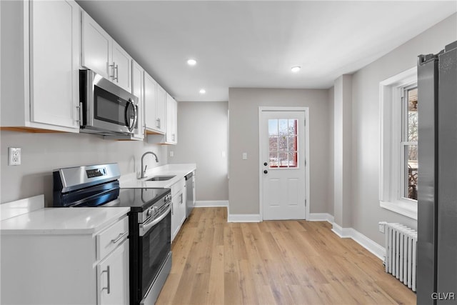 kitchen featuring white cabinetry, stainless steel appliances, light wood-type flooring, radiator, and sink