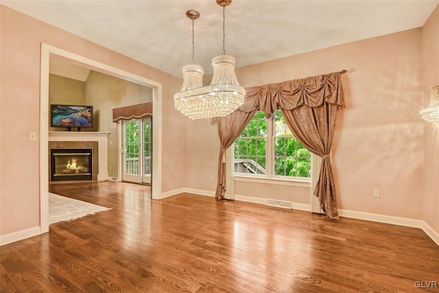 unfurnished dining area featuring hardwood / wood-style flooring, lofted ceiling, a chandelier, and a fireplace