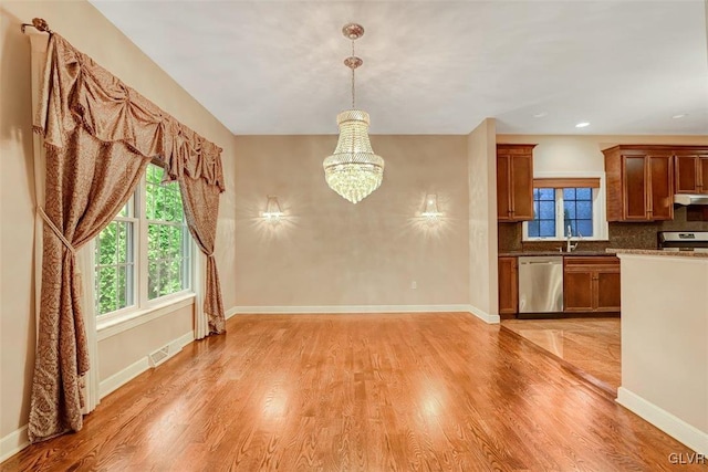 kitchen with decorative light fixtures, stainless steel appliances, tasteful backsplash, light hardwood / wood-style floors, and a notable chandelier