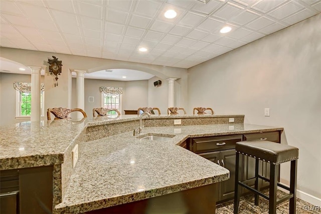 kitchen with light stone countertops, sink, ornate columns, and a breakfast bar