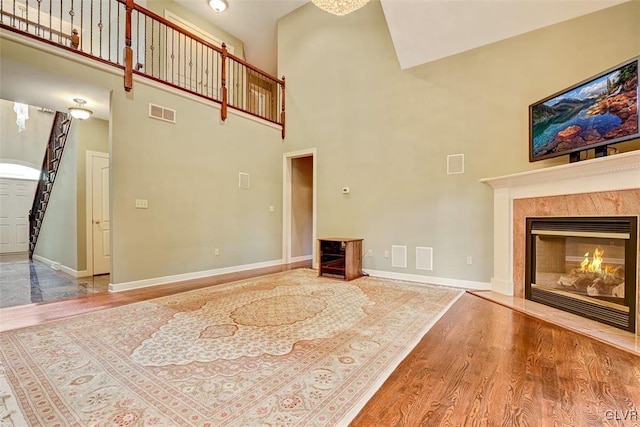 unfurnished living room with a high ceiling, wood-type flooring, and a high end fireplace