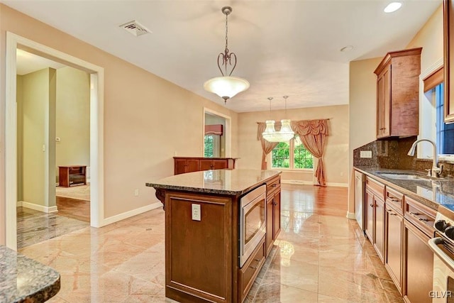 kitchen with appliances with stainless steel finishes, tasteful backsplash, a center island, decorative light fixtures, and sink