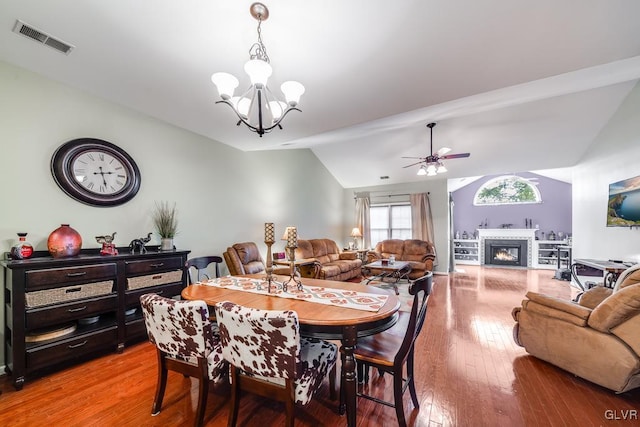 dining space with hardwood / wood-style floors, ceiling fan with notable chandelier, and vaulted ceiling