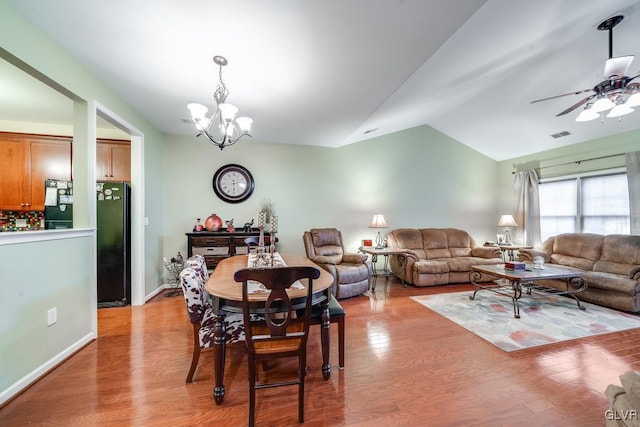 dining space with light hardwood / wood-style floors, ceiling fan with notable chandelier, and vaulted ceiling