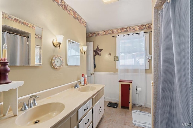 full bath featuring a wainscoted wall, tile patterned flooring, a wealth of natural light, and a sink