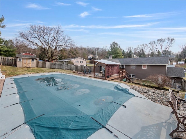 view of swimming pool featuring an outbuilding, a fenced backyard, a wooden deck, a fenced in pool, and a storage unit