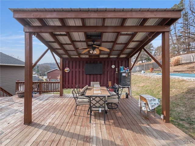 wooden terrace with a ceiling fan, outdoor dining area, and fence