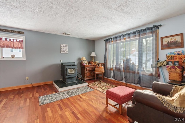 living area featuring a wood stove, visible vents, a textured ceiling, and wood finished floors