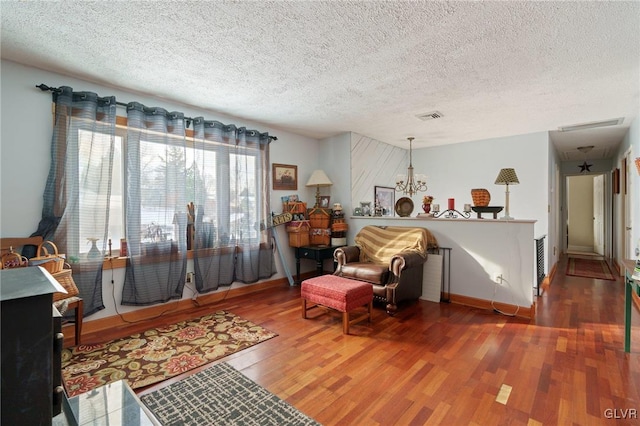 sitting room with a textured ceiling, wood finished floors, visible vents, and an inviting chandelier