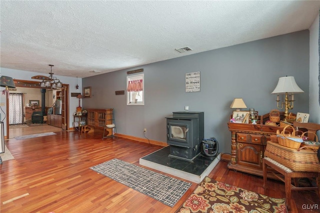 living area featuring a textured ceiling, wood finished floors, visible vents, baseboards, and a wood stove