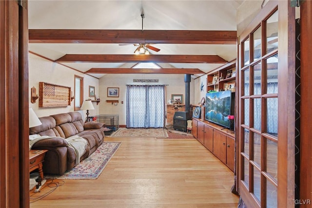 living room with a wood stove, light wood-type flooring, a ceiling fan, and beamed ceiling