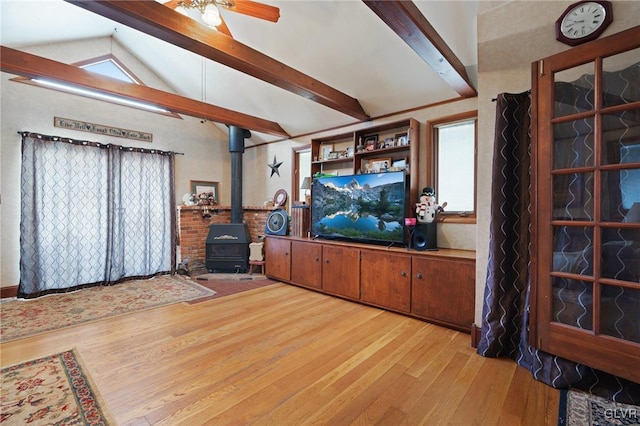 living room with lofted ceiling with beams, a wood stove, light wood-style flooring, and a ceiling fan