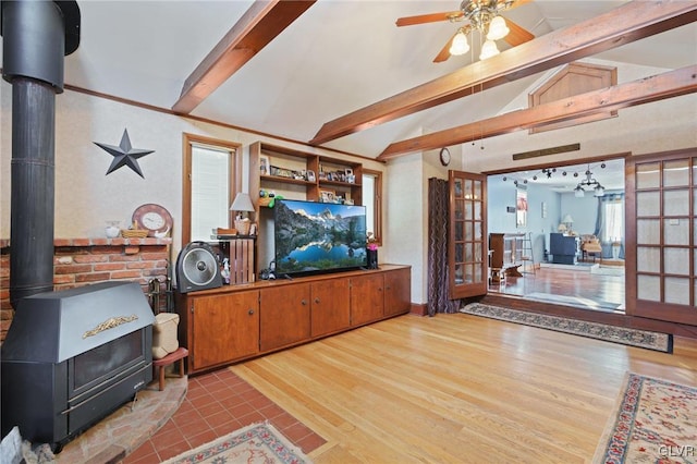 living room featuring light wood-style flooring, ceiling fan, a wood stove, vaulted ceiling with beams, and french doors